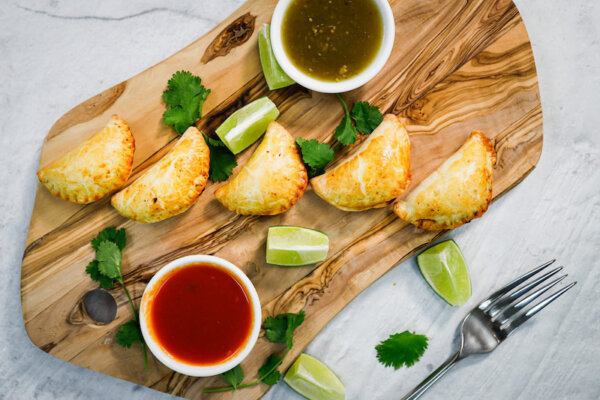 A tray of mini empanadas made with plant-based proteins and a chili-flavored sauce.