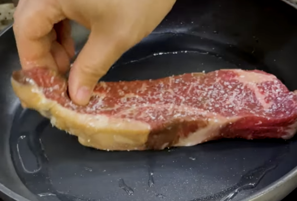 Chef Bryan putting a grass-fed steak, seasoned with salt, into a hot pan to sear.