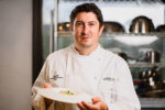 Portrait of Chef Ryan holding a plate of his Plant-Based Red Wine Braised Beef Cheek Ravioli, Griffith Foods