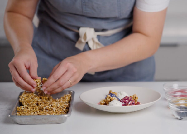 A close up of a chef's hands preparing granola in a baking tray