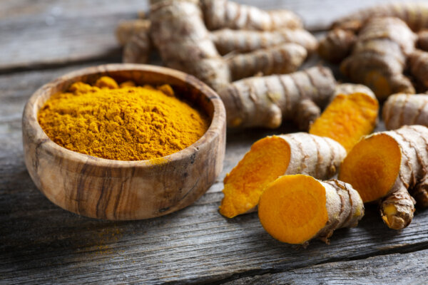 Fresh-cut turmeric root next to a wooden bowl with powdered turmeric