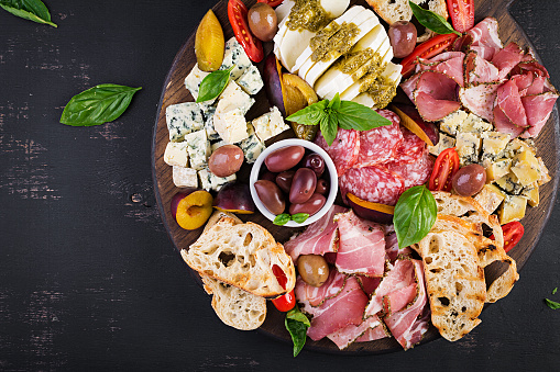 A shared platter of cured meats, cheeses, olives, bread, and fresh herbs, representing traditional flavors presented in a modern, communal dining style.