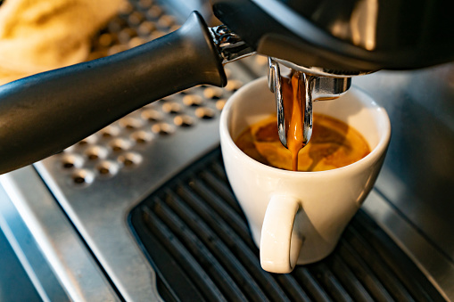 Espresso being extracted into a white cup from a coffee machine, reflecting familiar coffee rituals and the enduring appeal of classic flavors.