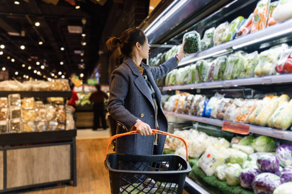Women selecting pre-packaged fresh greens in the produce aisle, reflecting how busy consumers prioritize convenient, ready-to-use food options that simplify the meal preparation.  