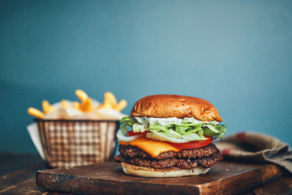 Close-up of a burger with layered textures crispy lettuce, melted cheese, and a soft bun—next to fries, illustrating how texture combinations shape perception in the food market. 