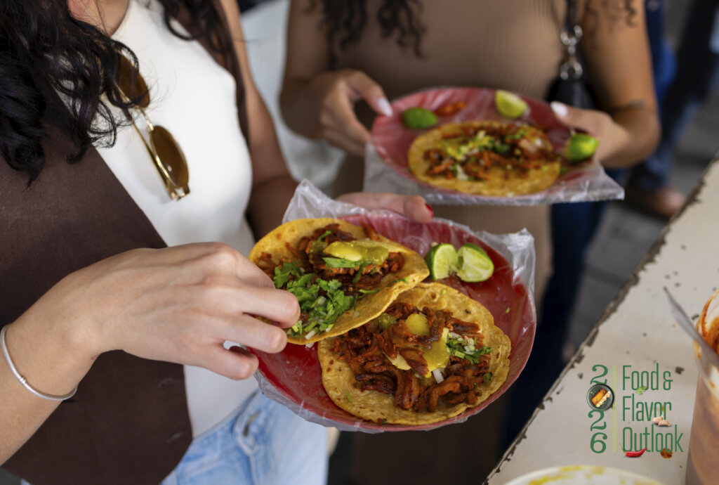 People holding street-style tacos topped with fresh ingredients, illustrating how globally inspired street foods become scalable menu concepts. 