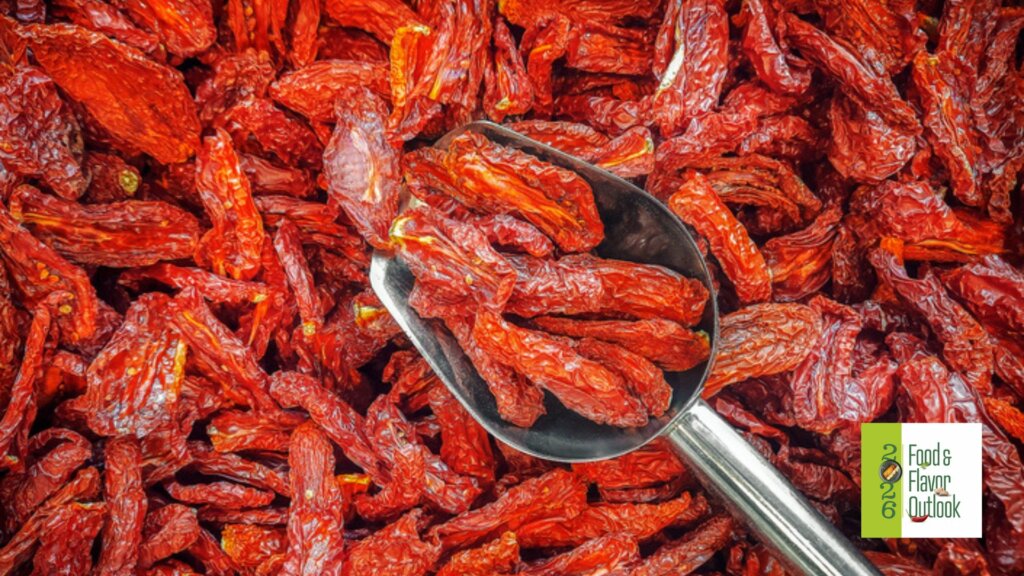 Close-up of bright red dried chili peppers pilled with a metal scoop, illustrating bold, spicy, maximalist flavors.