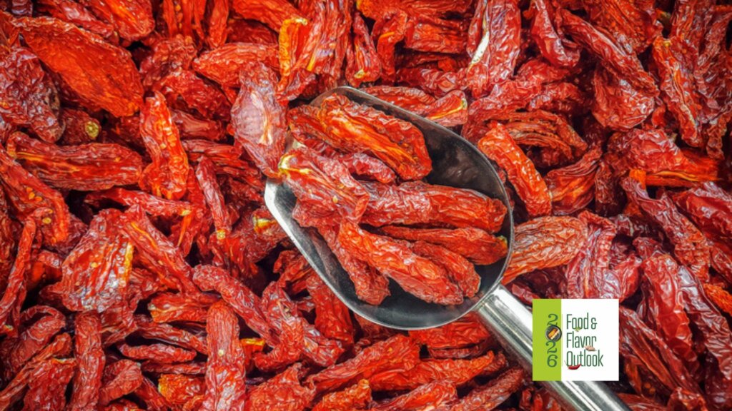 Close-up of bright red dried chili peppers pilled with a metal scoop, illustrating bold, spicy, maximalist flavors.