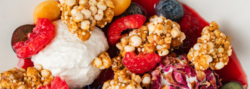 A sweet dessert with fruit compote, raspberries, blueberries, puffed quinoa, and flower petals.