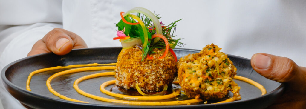 Two falafel balls made with ancient grains, served on a plate with drizzled sauce and garnished with herbs, flowers, and peppers.