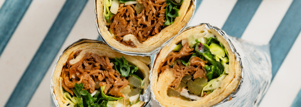 A shawarma pita wrap with shredded meat and lettuce, wrapped in tin foil.